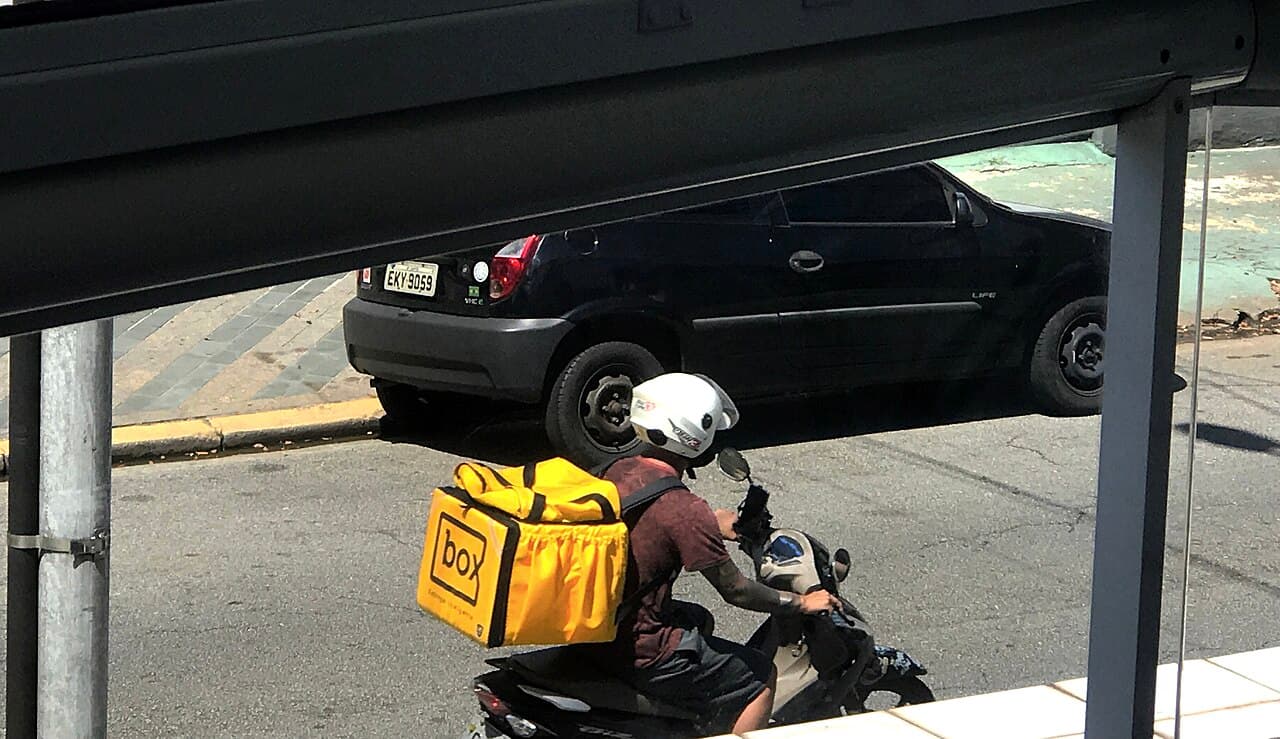 A delivery motorcycle with a box on the back riding through town